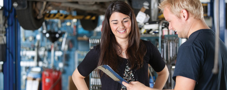 young mechanic and woman looking at notepad and smiling in garage