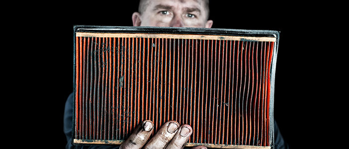 an auto mechanic holds up a filthy, grungy air filter removed from a car during normal maintenance