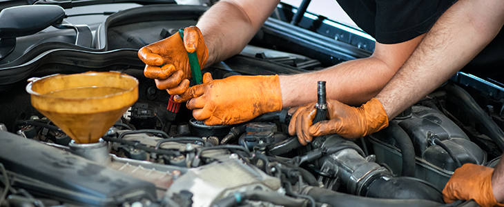 Two mechanics working on a vehicle in a garage or service workshop, close up of their gloved hands and equipment in the engine compartment