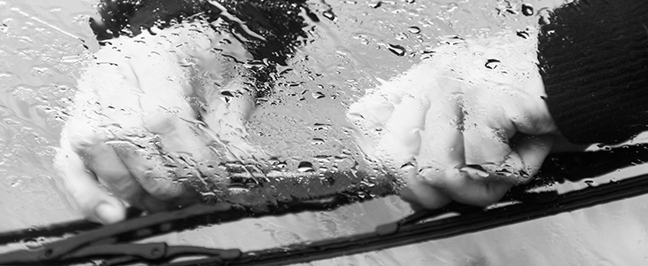 the man in the rain repairs a window wiper by car in black and w