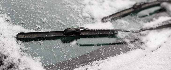 Car wiper blades clean snow from car windows. Flakes of snow covered the car with a thick layer. Safe driving with working wipers and clean windshield.